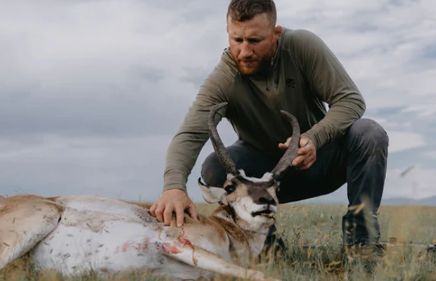 A man stands over a recently killed antelope.