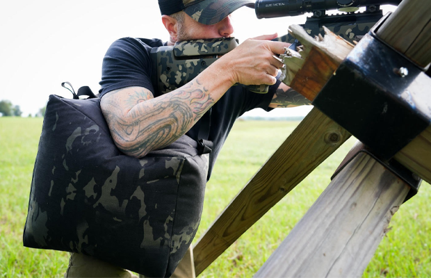 A man shooting a rifle with a sling bag.