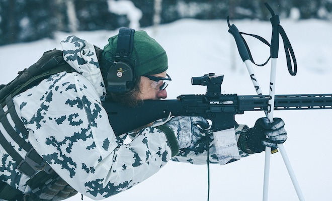 Man shooting a rifle in the snow.